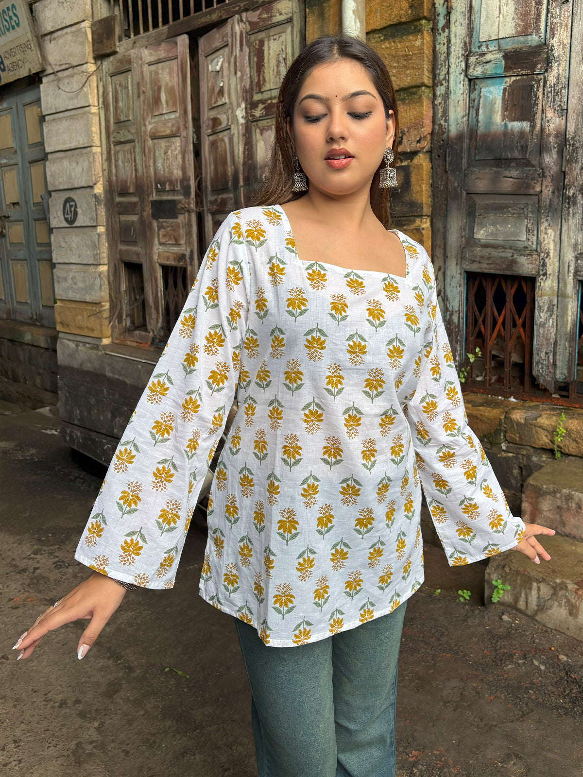 Woman wearing a white floral blouse with yellow flowers in an outdoor setting.